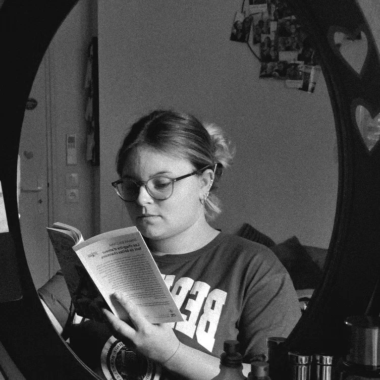 Lisa, en noir et blanc, lit un roman, reflétée dans un grand miroir rond.